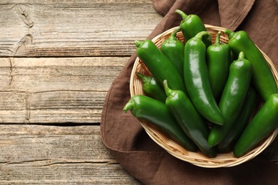Photo of Ripe green jalapeno peppers in basket and towel on wooden table, top view. Space for text