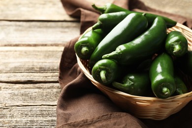 Photo of Ripe green jalapeno peppers in basket and towel on wooden table, closeup. Space for text