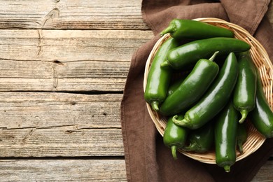 Photo of Ripe green jalapeno peppers in basket and towel on wooden table, top view. Space for text