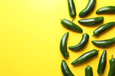Photo of Green jalapeno peppers on yellow background, flat lay. Space for text