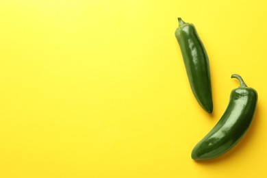 Photo of Green jalapeno peppers on yellow background, flat lay. Space for text