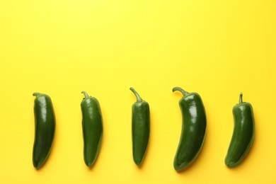 Photo of Green jalapeno peppers on yellow background, flat lay. Space for text