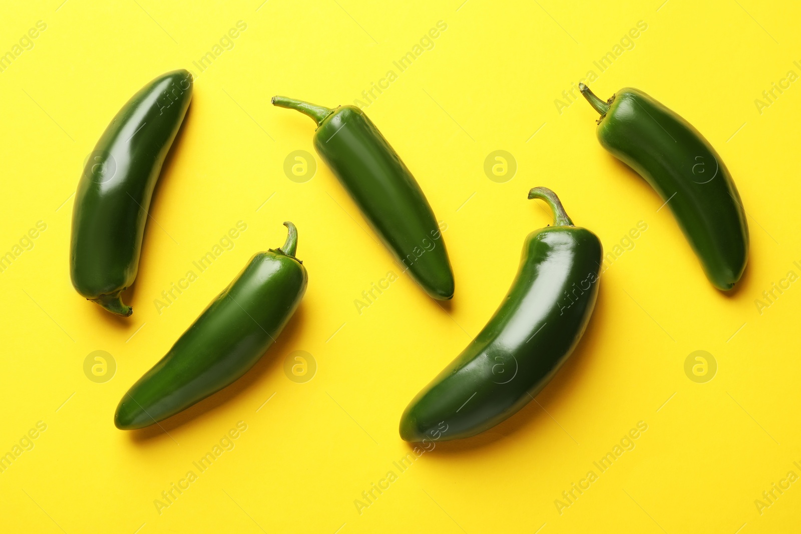 Photo of Green jalapeno peppers on yellow background, flat lay