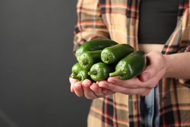 Photo of Woman with ripe green jalapeno peppers on black background, closeup. Space for text