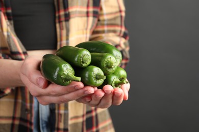 Photo of Woman with ripe green jalapeno peppers on black background, closeup. Space for text