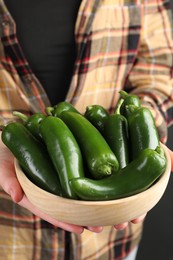 Photo of Woman with ripe green jalapeno peppers on black background, closeup