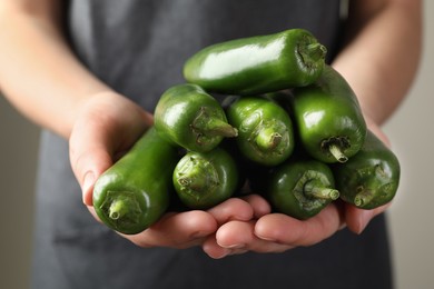 Photo of Woman with ripe green jalapeno peppers on light background, closeup