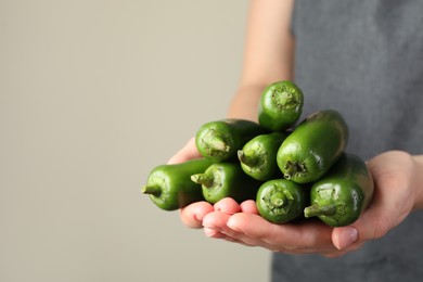 Photo of Woman with ripe green jalapeno peppers on light background, closeup. Space for text