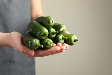 Photo of Woman with ripe green jalapeno peppers on light background, closeup