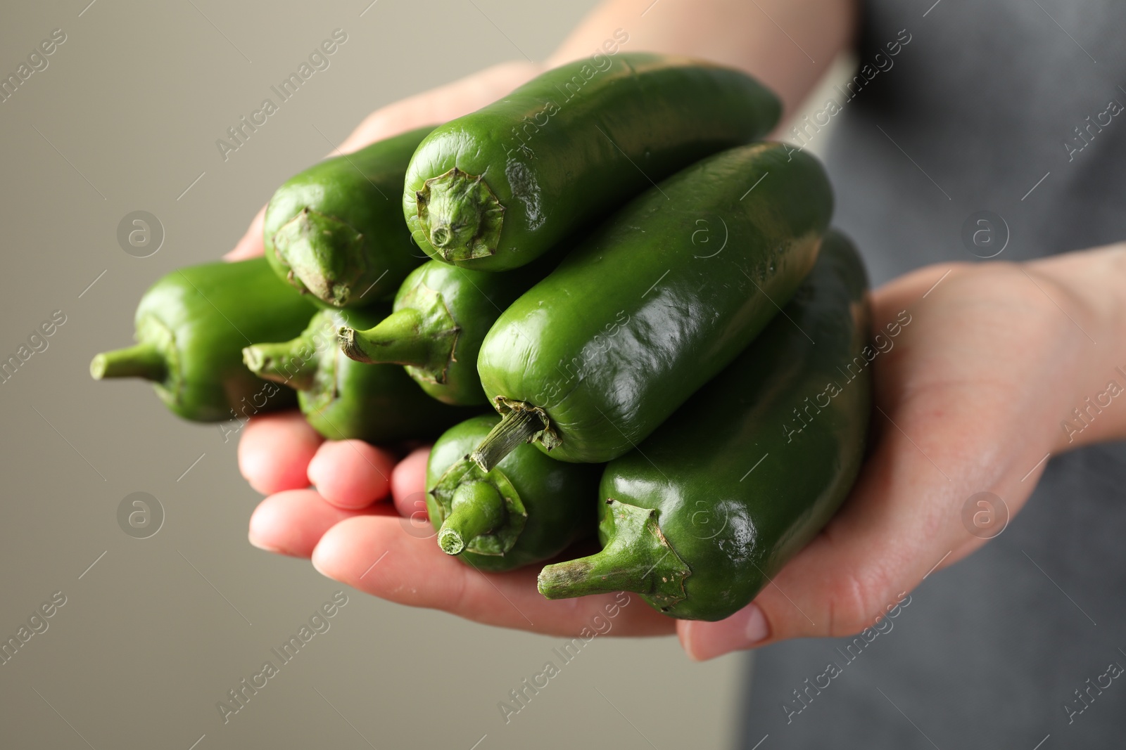 Photo of Woman with ripe green jalapeno peppers on light background, closeup