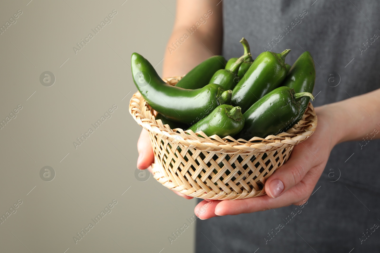 Photo of Woman with ripe green jalapeno peppers on light background, closeup. Space for text