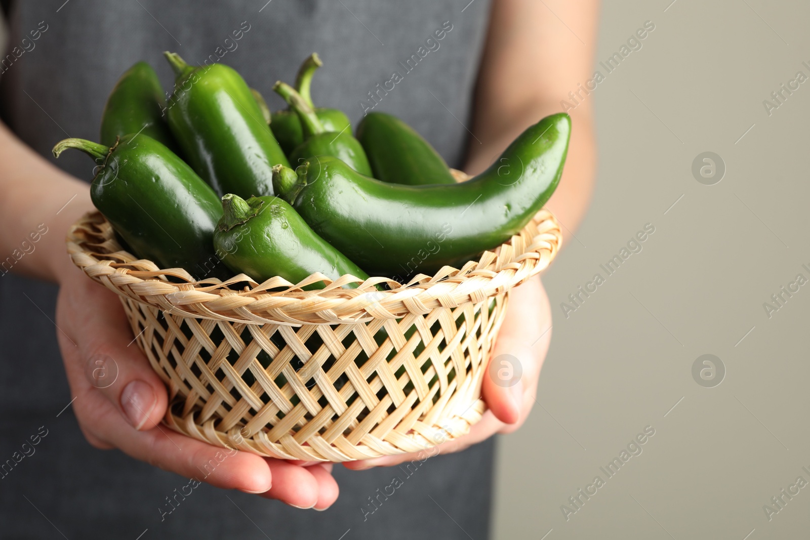Photo of Woman with ripe green jalapeno peppers on light background, closeup