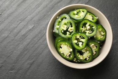 Photo of Pieces of green jalapeno peppers in bowl on grey table, top view. Space for text