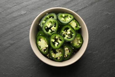 Photo of Pieces of green jalapeno peppers in bowl on grey table, top view