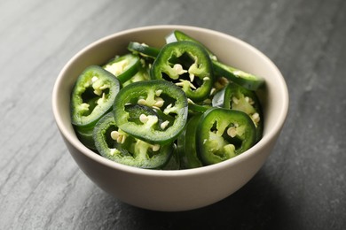 Photo of Pieces of green jalapeno peppers in bowl on grey table, closeup