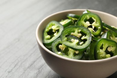 Photo of Pieces of green jalapeno peppers in bowl on grey table, closeup. Space for text