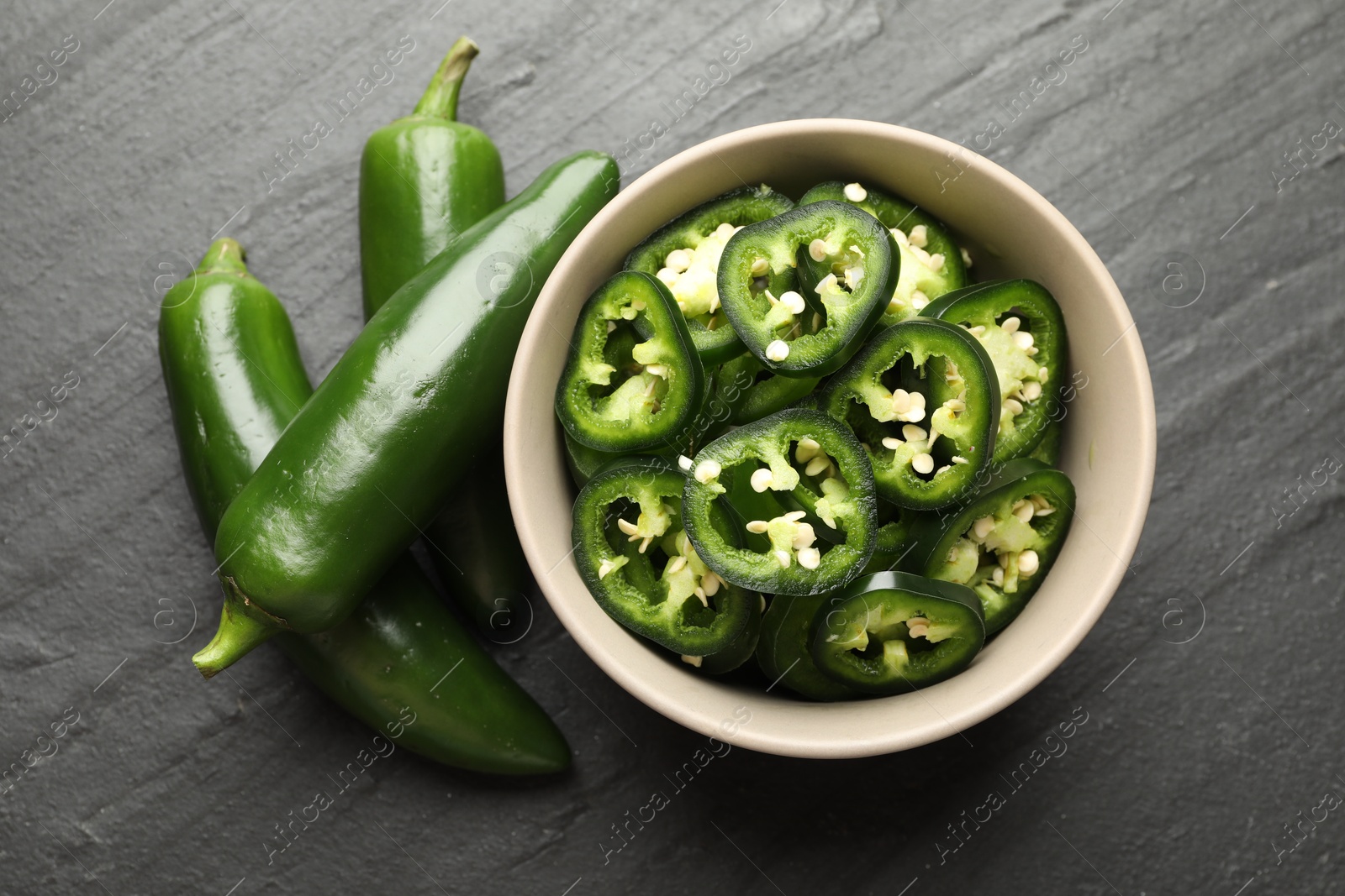 Photo of Whole and cut green jalapeno peppers on grey table, flat lay