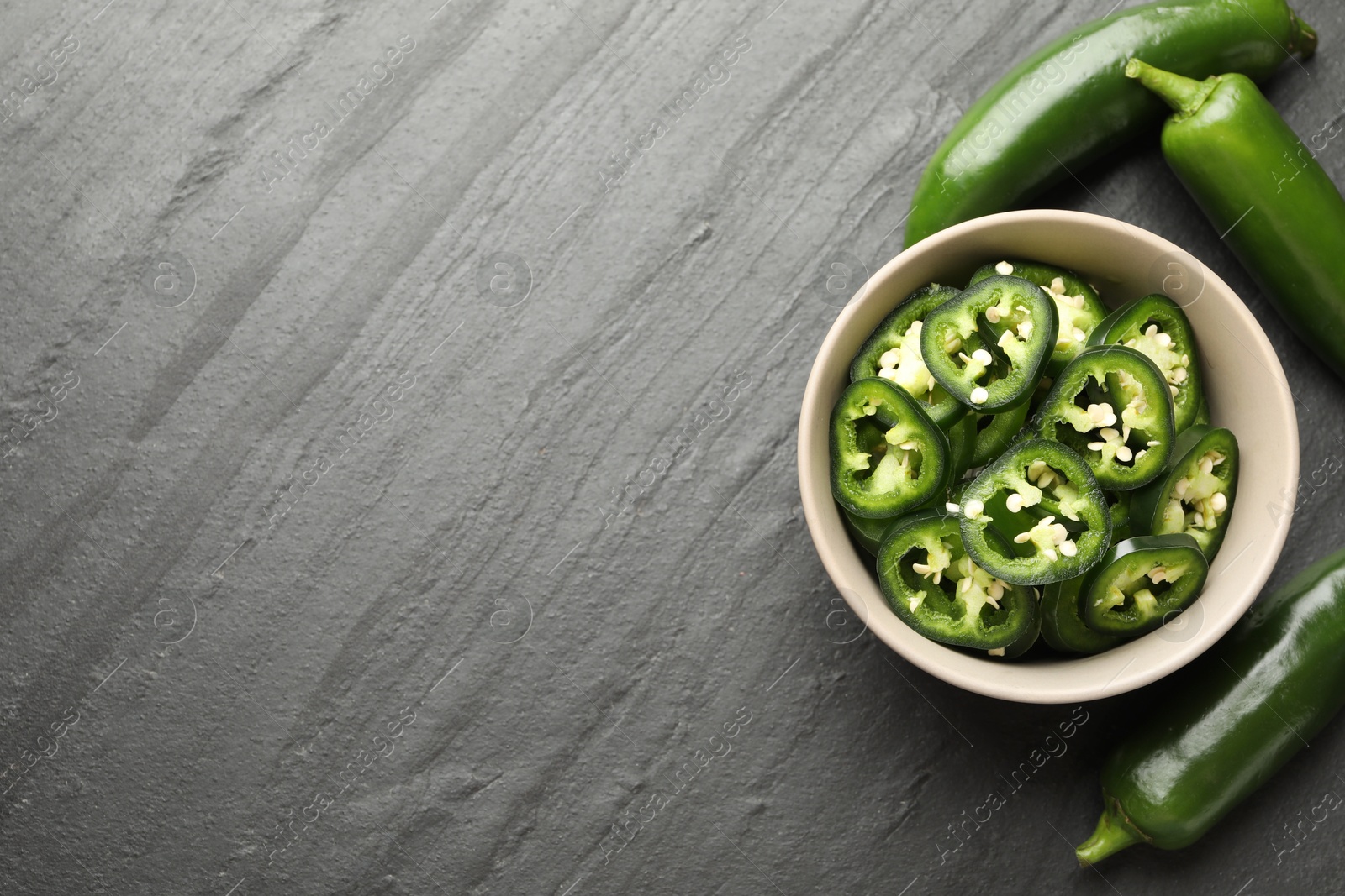 Photo of Whole and cut green jalapeno peppers on grey table, flat lay. Space for text