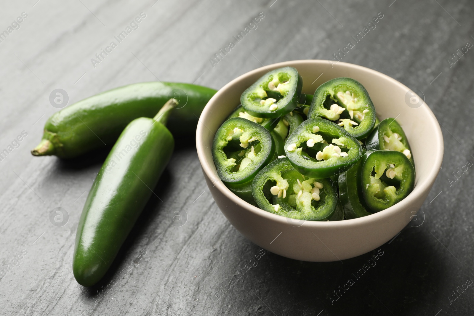 Photo of Whole and cut green jalapeno peppers on grey table, closeup