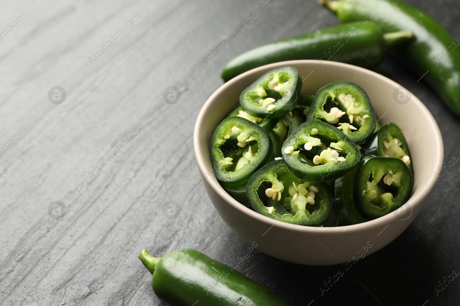 Photo of Whole and cut green jalapeno peppers on grey table, closeup. Space for text
