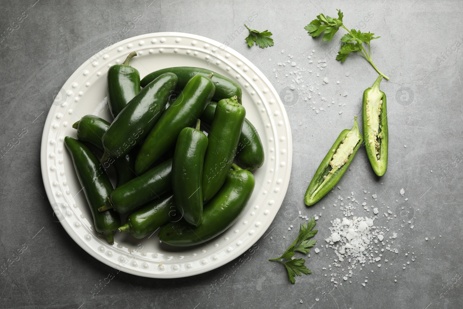 Photo of Ripe green jalapeno peppers, parsley and salt on grey table, flat lay