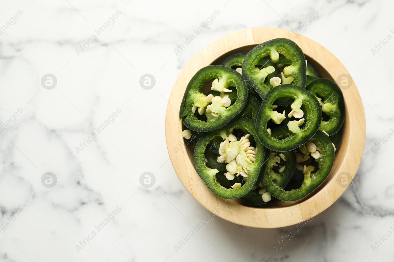 Photo of Pieces of green jalapeno peppers in bowl on white marble table, top view. Space for text