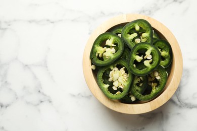 Photo of Pieces of green jalapeno peppers in bowl on white marble table, top view. Space for text