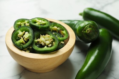 Photo of Whole and cut jalapeno peppers on white marble table, closeup