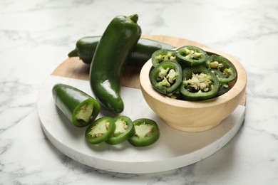 Photo of Whole and cut jalapeno peppers on white marble table, closeup