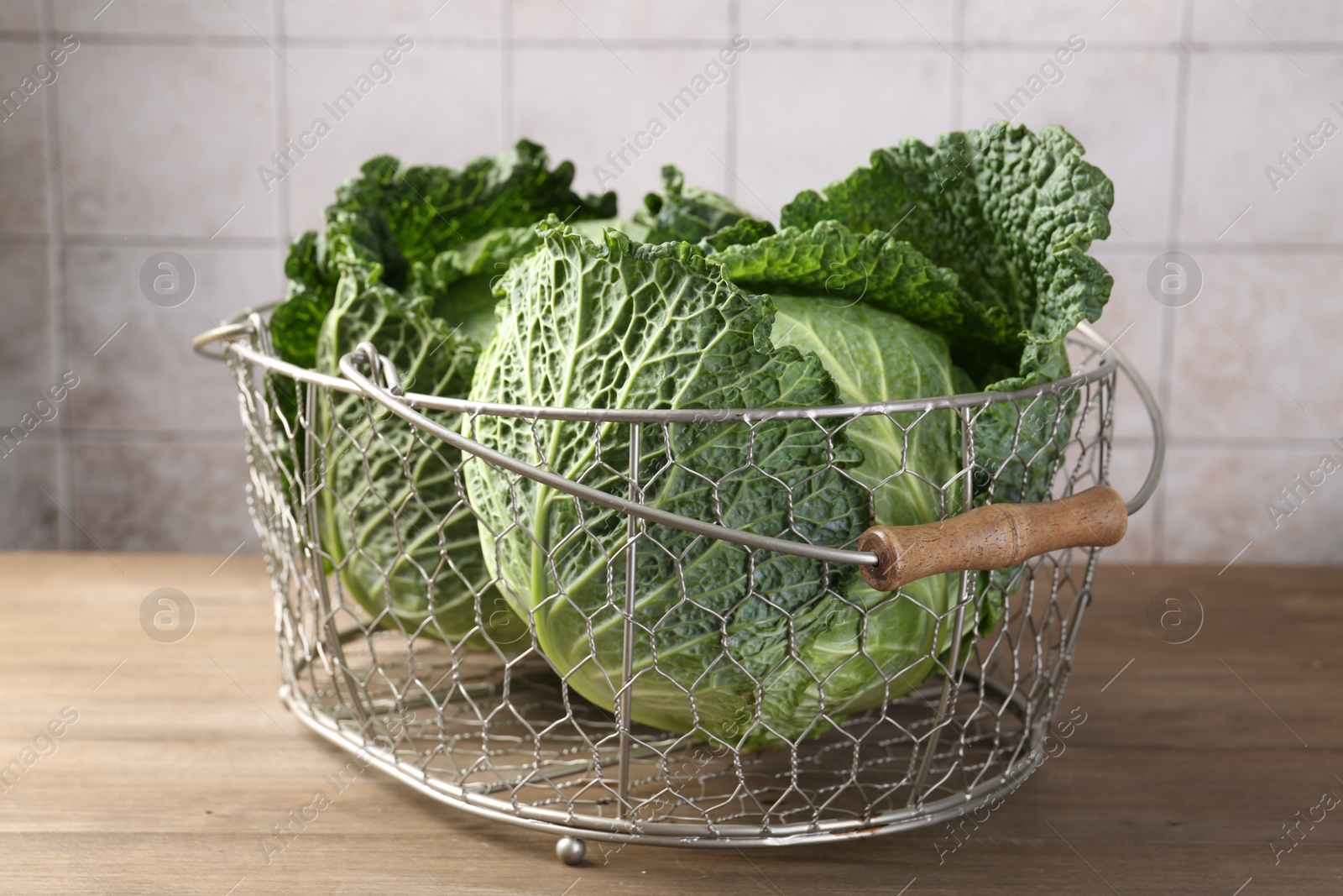 Photo of Fresh Savoy cabbages in metal basket on wooden table, closeup
