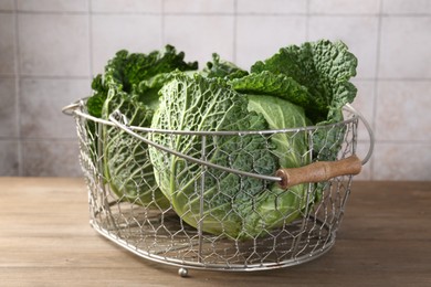 Photo of Fresh Savoy cabbages in metal basket on wooden table, closeup