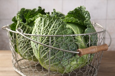 Photo of Fresh Savoy cabbages in metal basket on wooden table, closeup