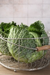 Photo of Fresh Savoy cabbages in metal basket on wooden table, closeup