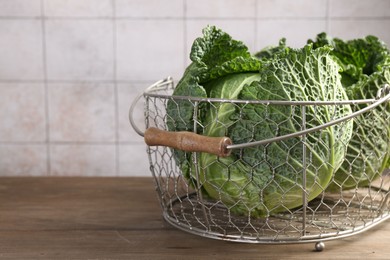 Photo of Fresh Savoy cabbages in metal basket on wooden table, closeup. Space for text