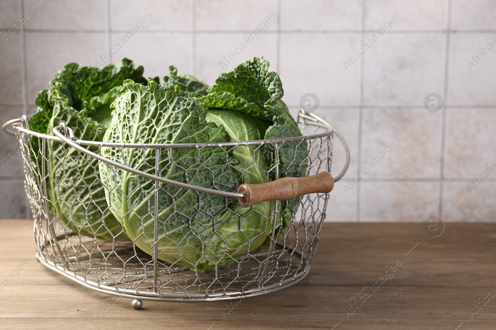 Photo of Fresh Savoy cabbages in metal basket on wooden table, closeup. Space for text