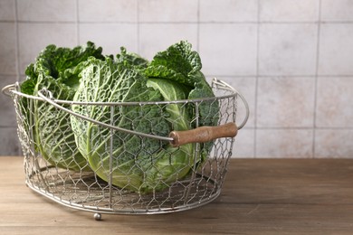 Photo of Fresh Savoy cabbages in metal basket on wooden table, closeup. Space for text