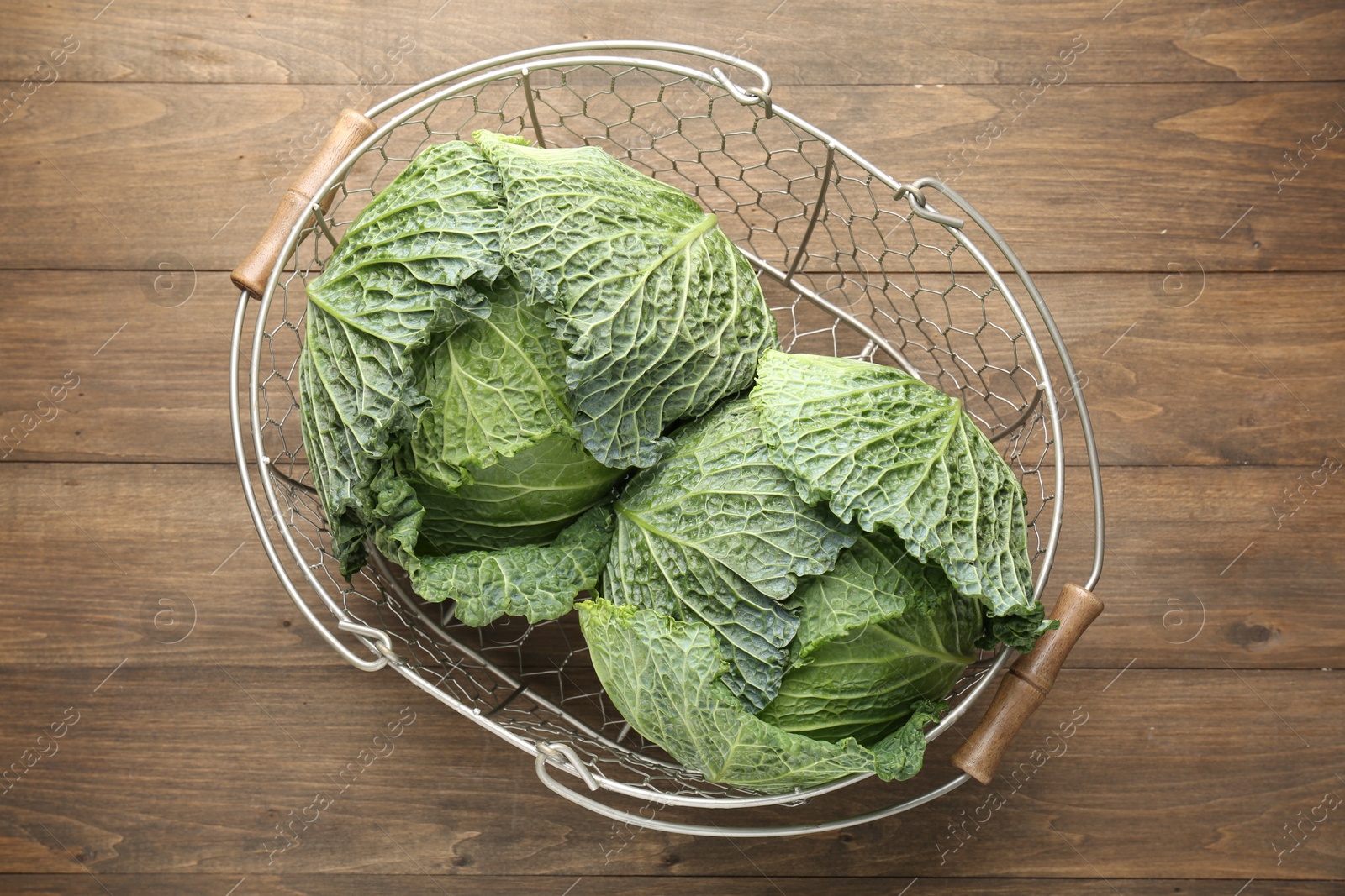 Photo of Fresh Savoy cabbages in metal basket on wooden table, top view