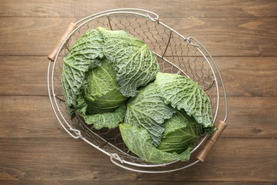 Photo of Fresh Savoy cabbages in metal basket on wooden table, top view