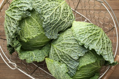 Photo of Fresh Savoy cabbages in metal basket on wooden table, top view