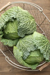 Photo of Fresh Savoy cabbages in metal basket on wooden table, top view