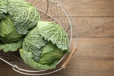 Photo of Fresh Savoy cabbages in metal basket on wooden table, top view. Space for text