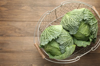 Photo of Fresh Savoy cabbages in metal basket on wooden table, top view. Space for text