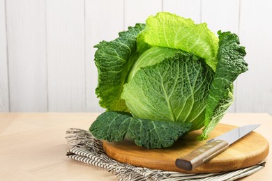 Photo of Fresh Savoy cabbage and knife on wooden table, closeup. Space for text