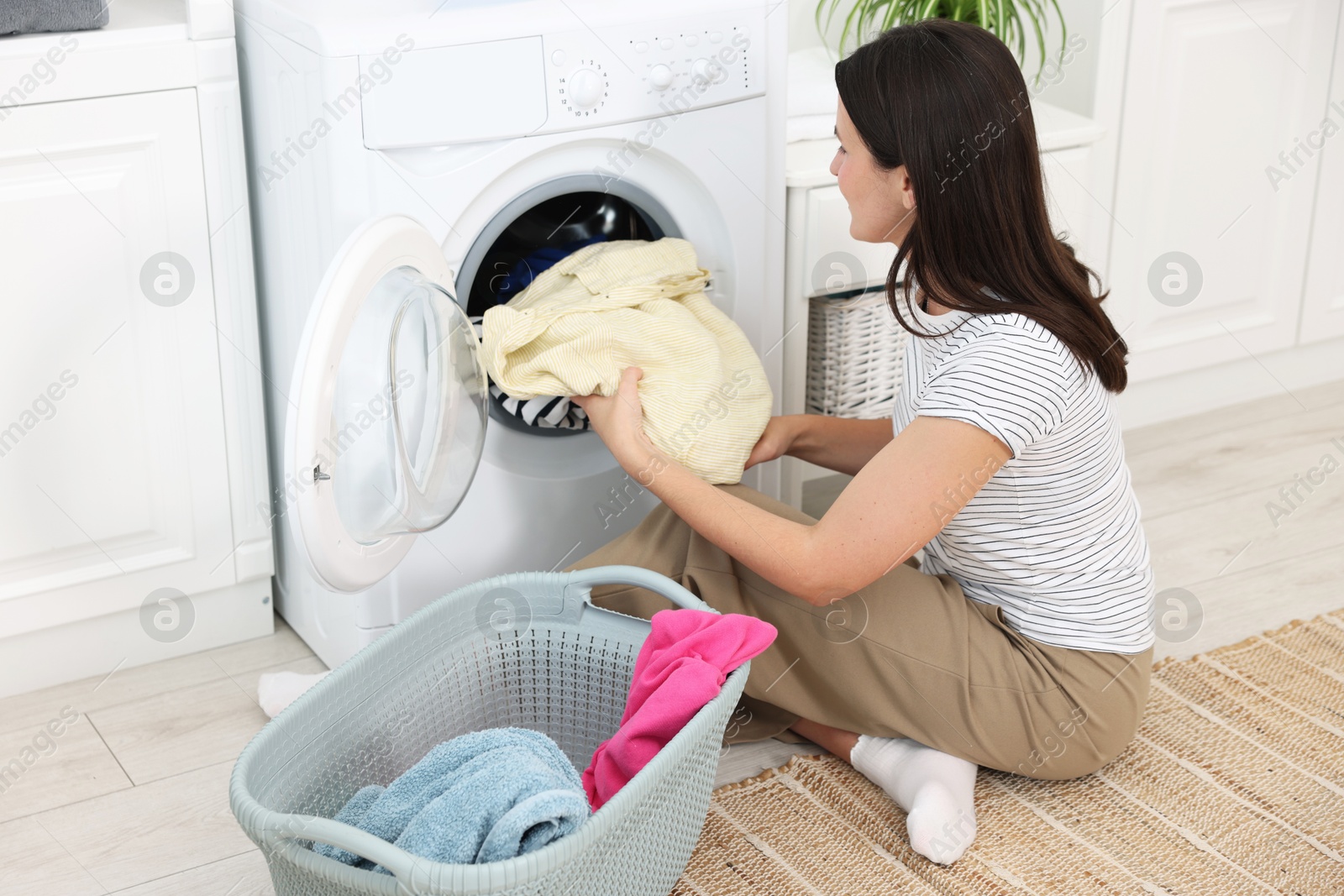 Photo of Woman taking laundry out of washing machine indoors