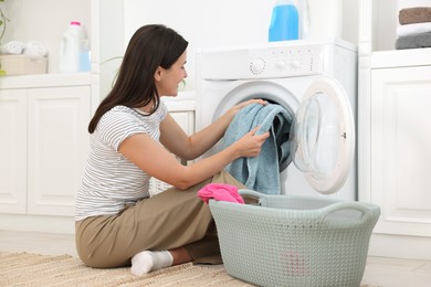 Photo of Woman taking laundry out of washing machine indoors