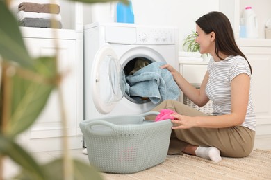 Photo of Woman taking laundry out of washing machine indoors
