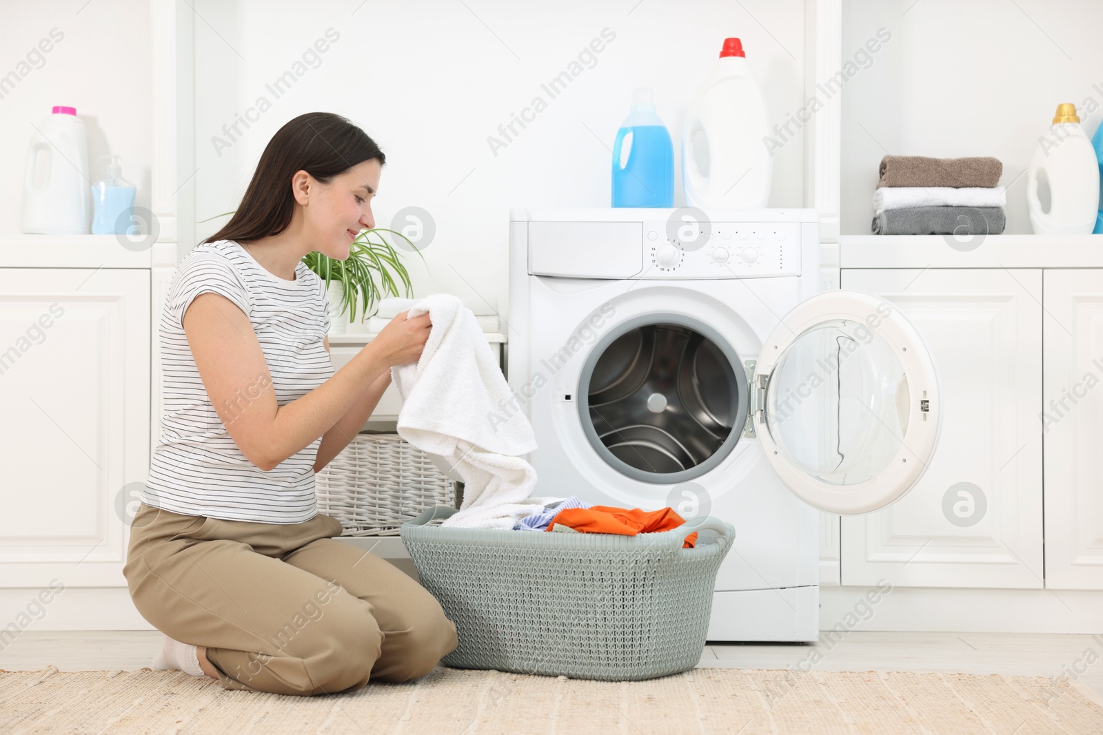 Woman with laundry near washing machine indoors Photo of Woman with laundry near washing machine indoors