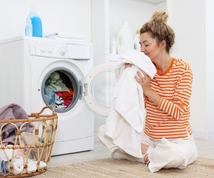 Photo of Happy woman with laundry near washing machine indoors