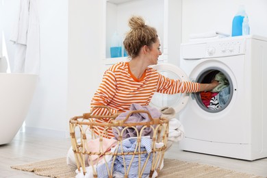 Photo of Woman putting dirty laundry into washing machine indoors