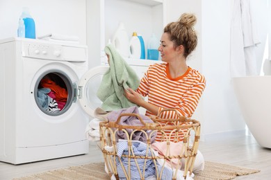 Photo of Happy woman with laundry near washing machine indoors